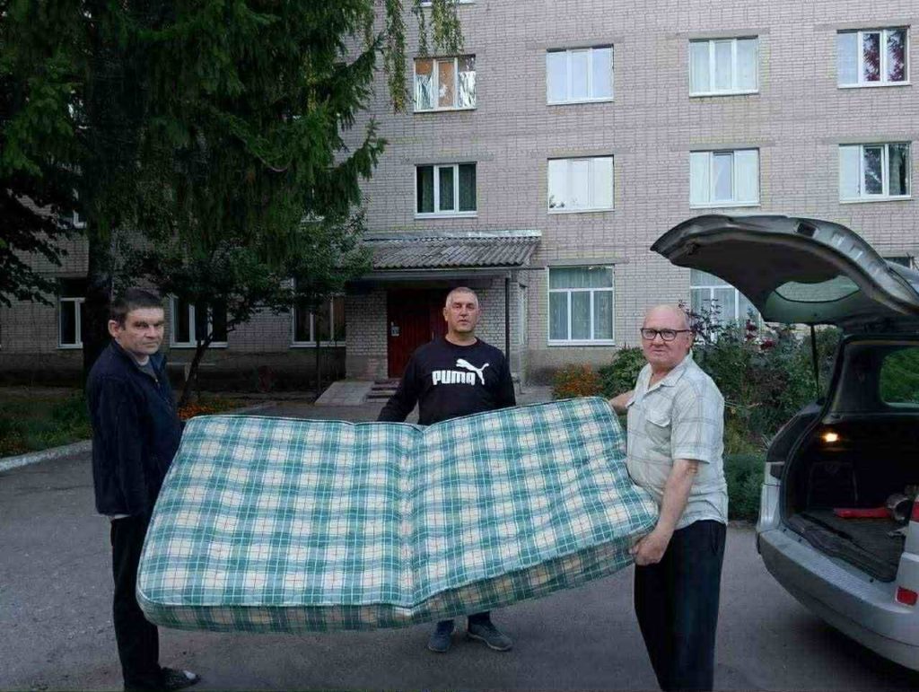 Three men carry a large mattress outside an apartment building.
