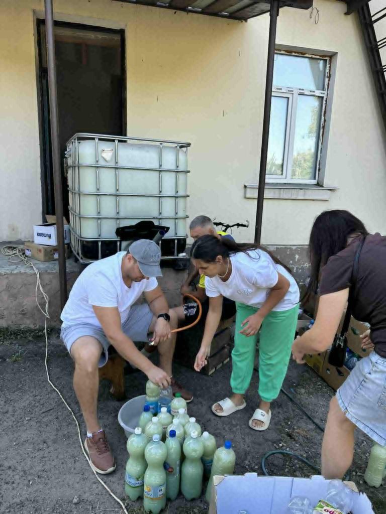 Volunteers fill plastic bottles with shampoo outdoors, preparing them for distribution.