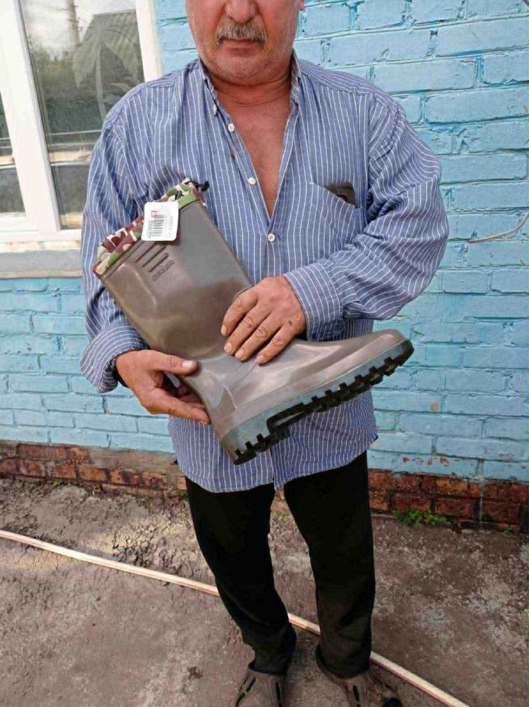 Man holding a new pair of sturdy rubber boots provided as aid