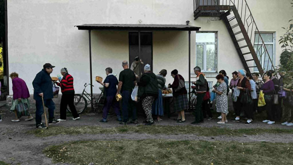 Long queue of people standing outside a building to collect free bread and food supplies.