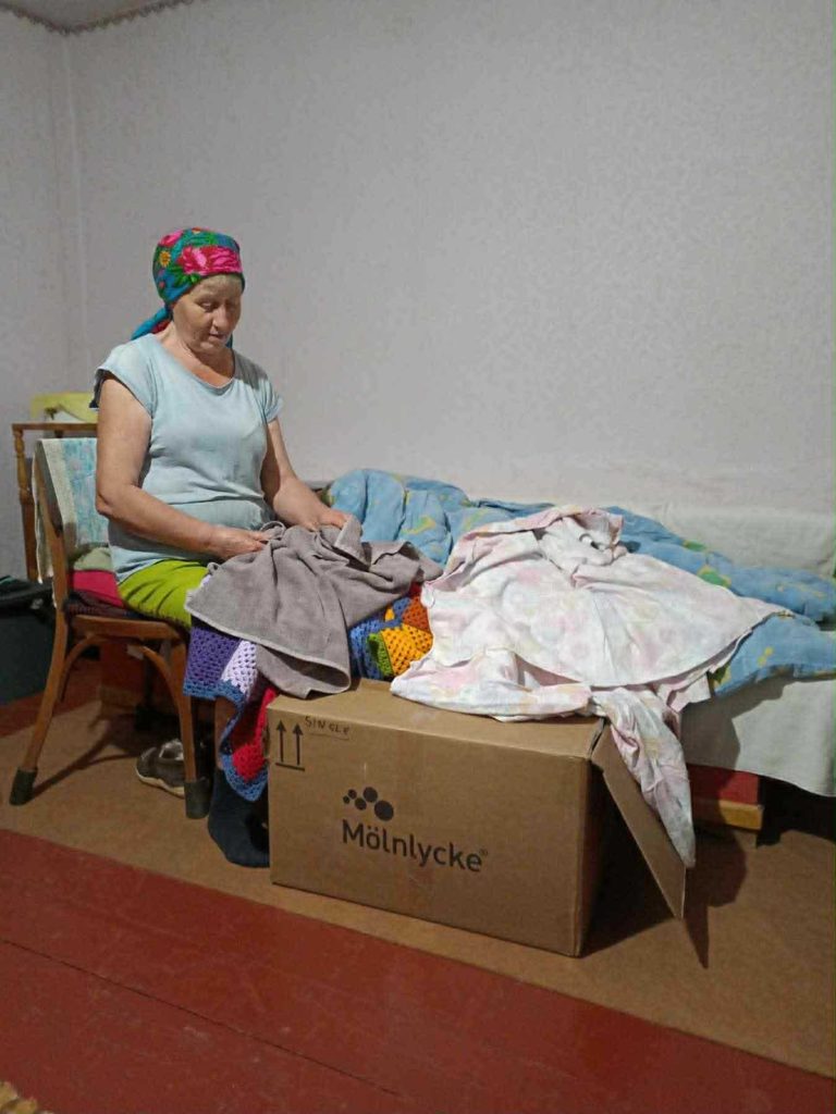 Woman sitting on a chair sewing bedding items next to a box of supplies