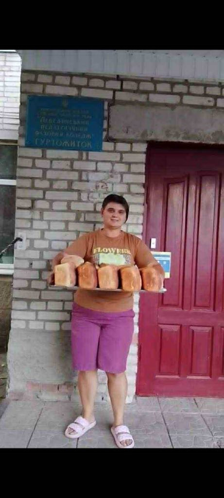 Woman standing outside holding a tray with loaves of bread for distribution to refugees.