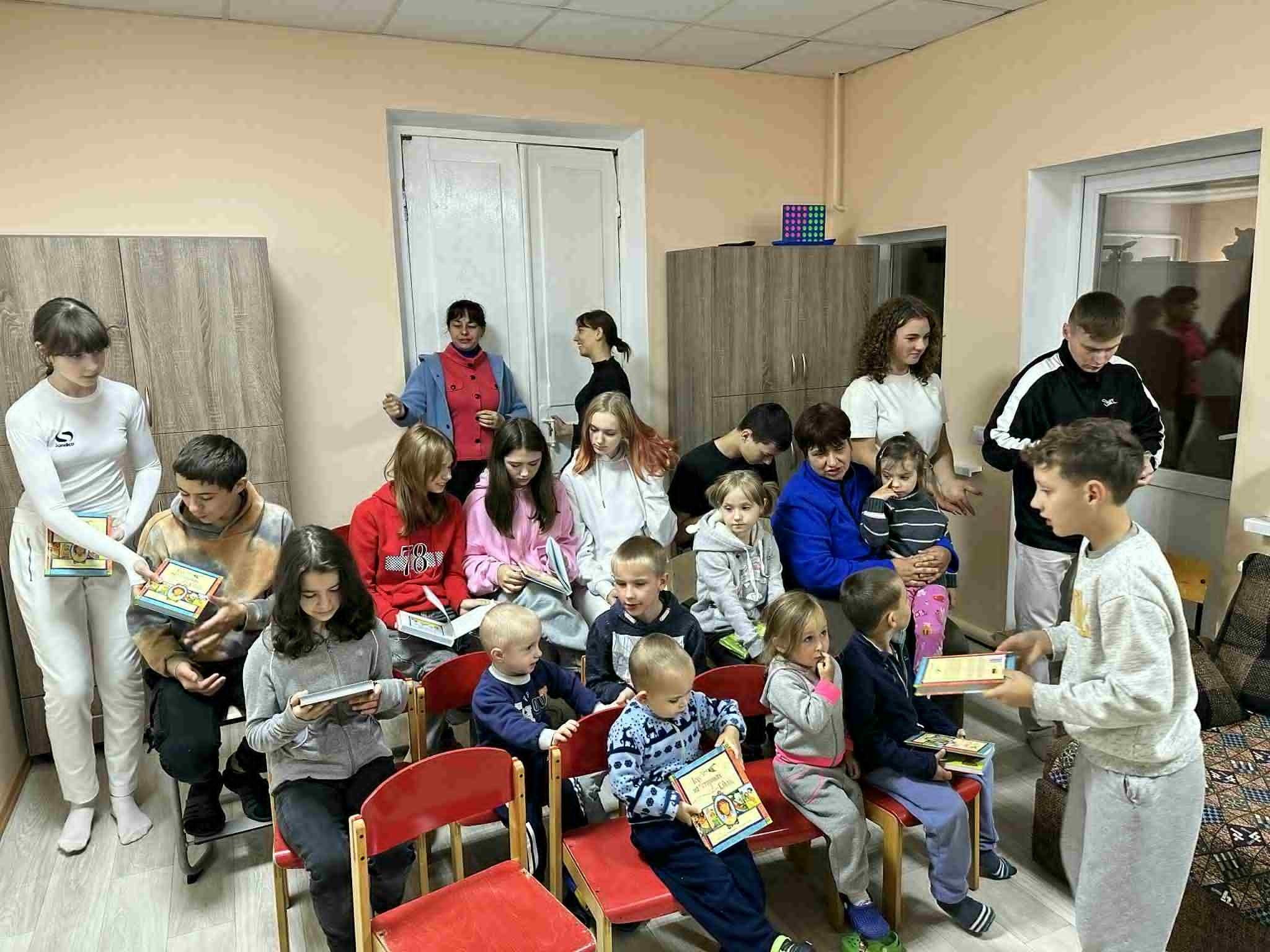 Children and volunteers gathered at a local hospital, sitting on red chairs while receiving donated copies of The Jesus Storybook Bible