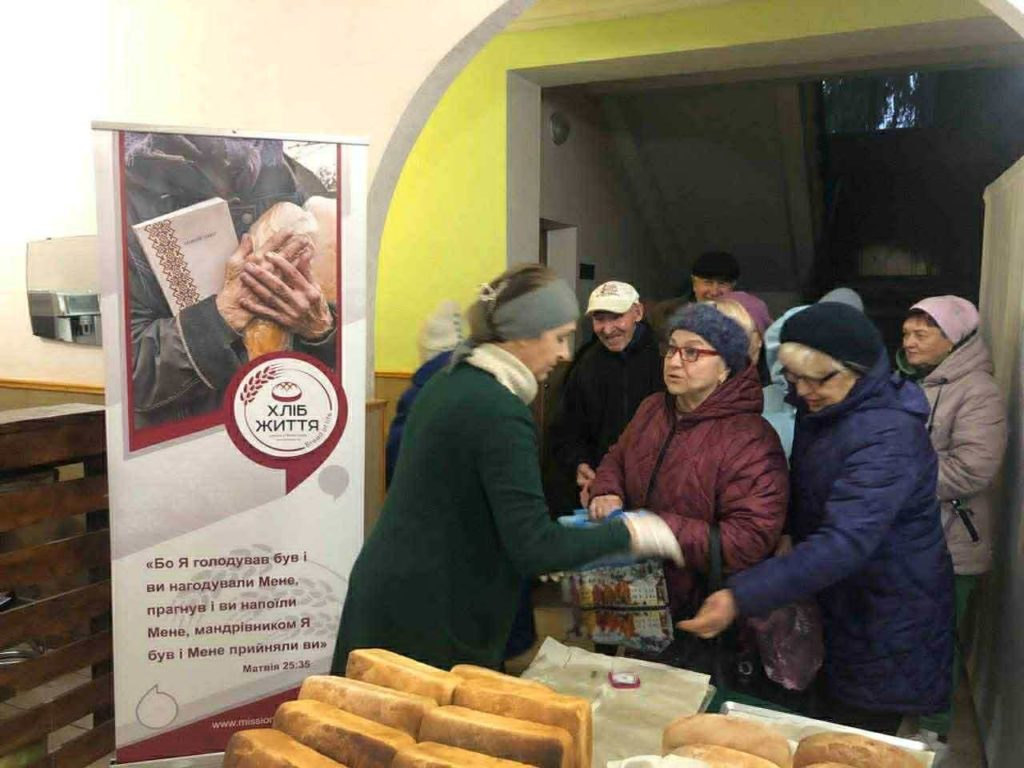 Volunteers at the Centre distributing fresh loaves of bread to elderly people lined up inside the building.