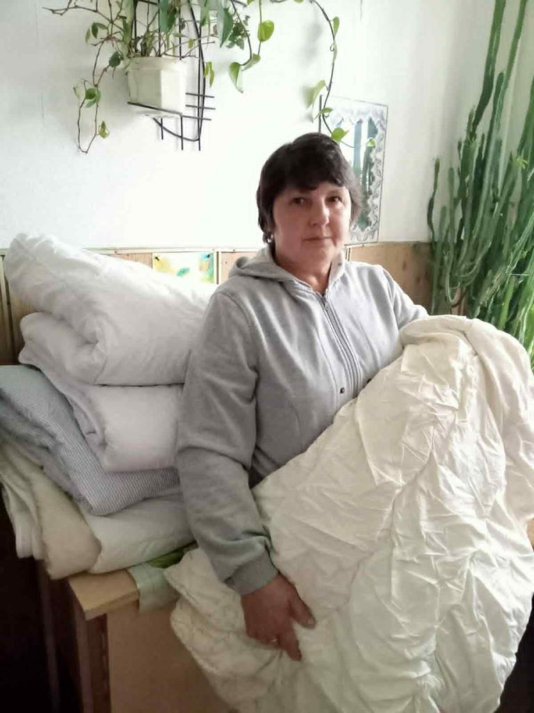 Woman standing indoors holding folded donated bedding and blankets.