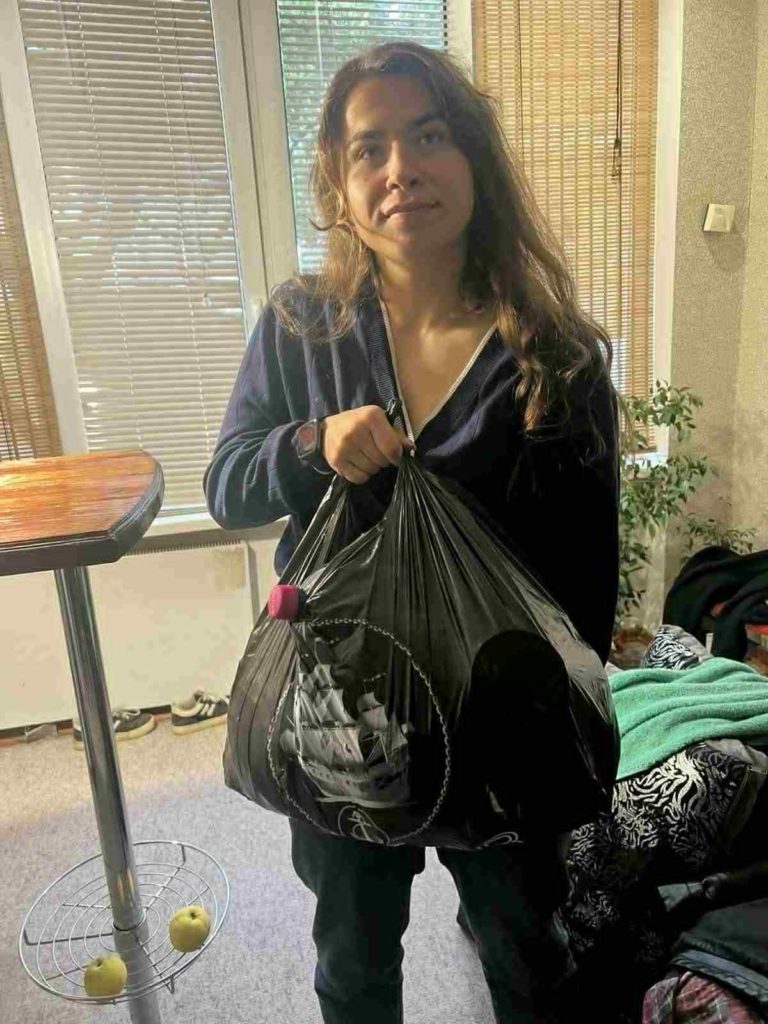 Woman standing indoors holding a large black bag of donated food aid, with gratitude on her face.