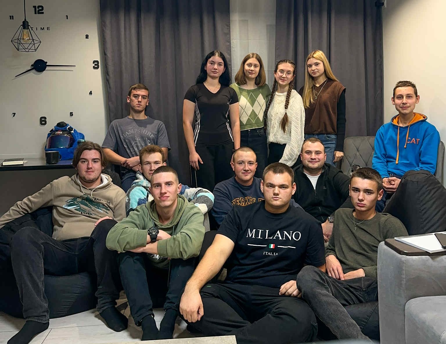 A group of young adults gathered in a living room for a home fellowship meeting, sitting together and smiling for the camera.