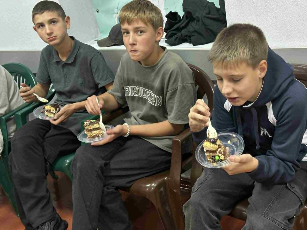 Three teenage boys sitting together enjoying slices of cake at a youth club event.