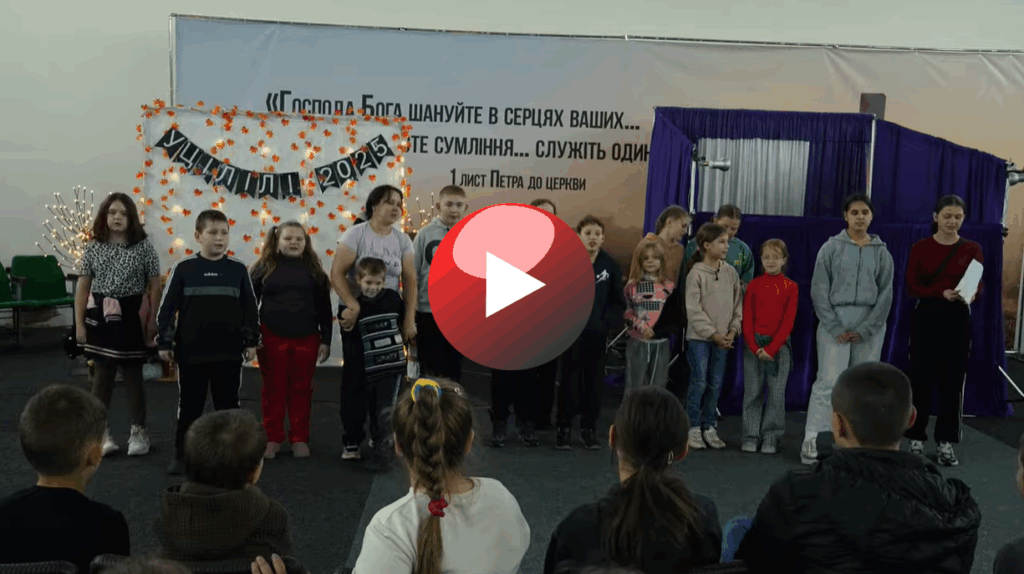 A group of children standing at the front of a room during the Autumn Camp 2025 event, performing together while other children watch from their seats.