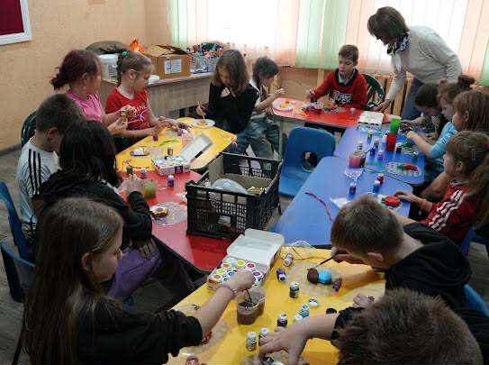 Group of children sitting around colourful tables painting and crafting together during an autumn camp activity.