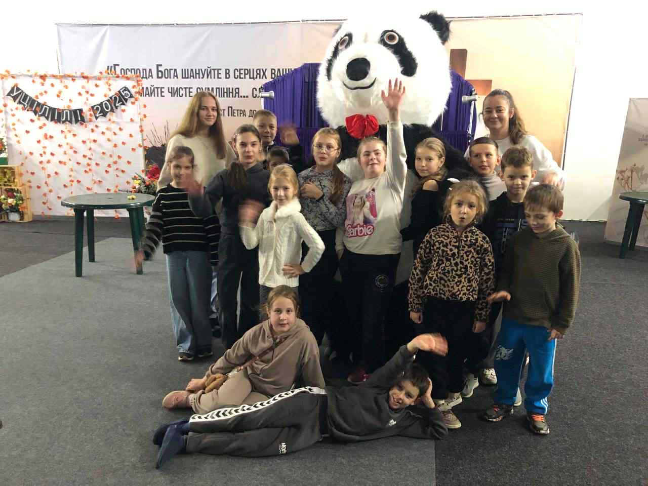 Group of children and camp leaders posing happily with a person in a giant panda costume during an autumn camp celebration.