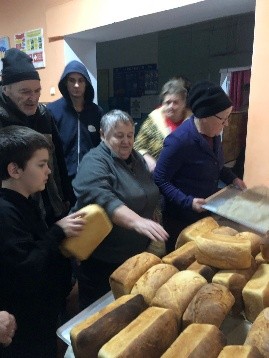 Adults and children inside the Centre receive loaves of bread from volunteers at a crowded distribution table.