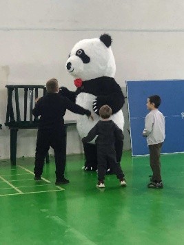 Children playing with a person dressed in a giant panda costume in the hall at the Centre