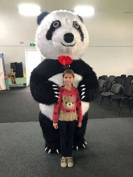 Young girl standing in front of a person wearing a giant panda costume inside the Centre.