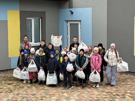 Group of children and adults standing outside a building holding distributed aid bags.
