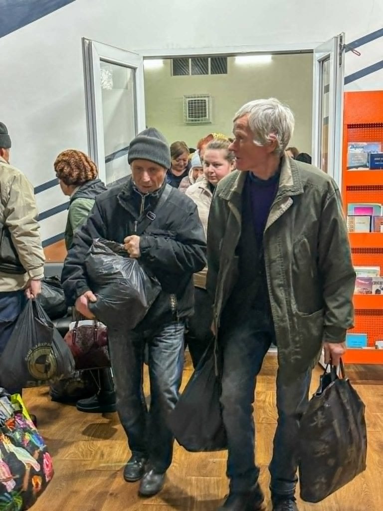 Two men walking through the Centre carrying black bags of humanitarian aid