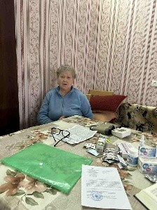 Tatyana sitting at a table covered with documents and medication.
