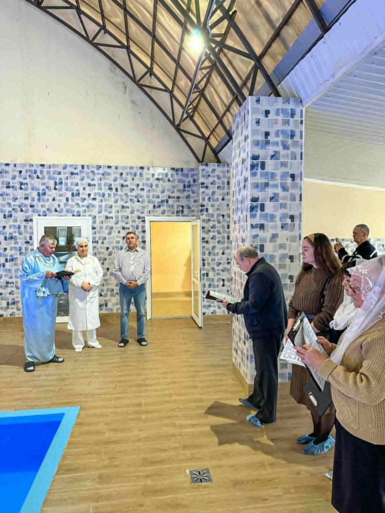 A group of church members gathered beside an indoor pool as a Pastor Sergey prepares for a baptism ceremony.