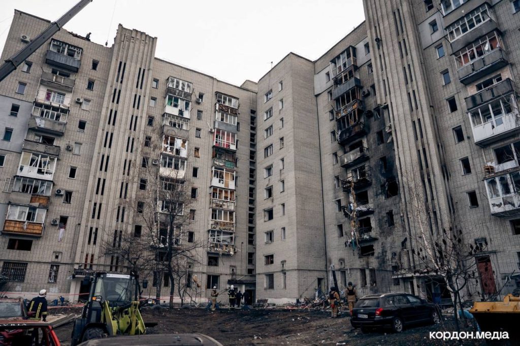 Heavily damaged apartment building in Okhtyrka after Russian shelling, with emergency workers on the scene.