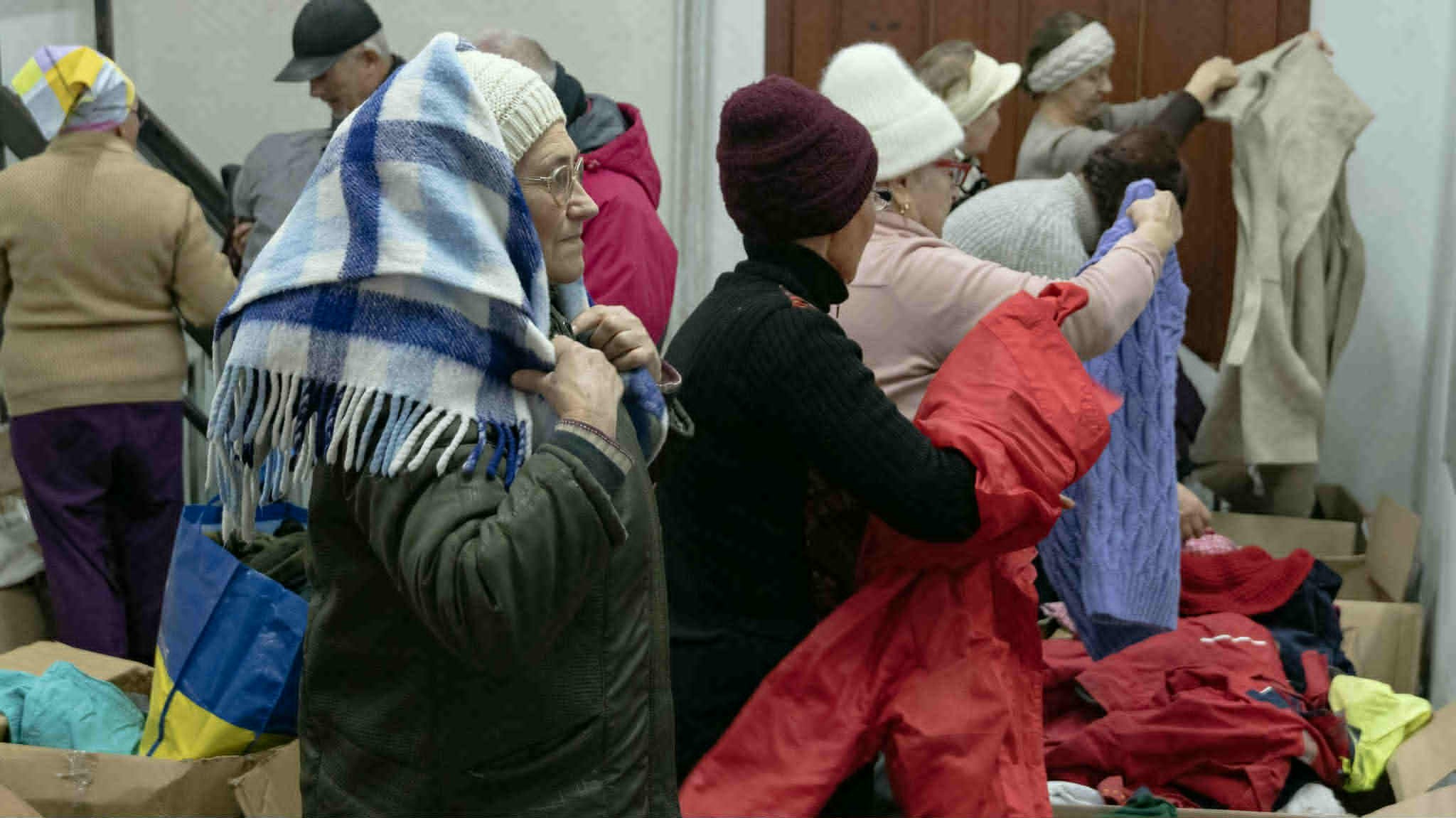 Elderly women examining donated winter clothing, scarves, and jackets during a community clothing distribution.