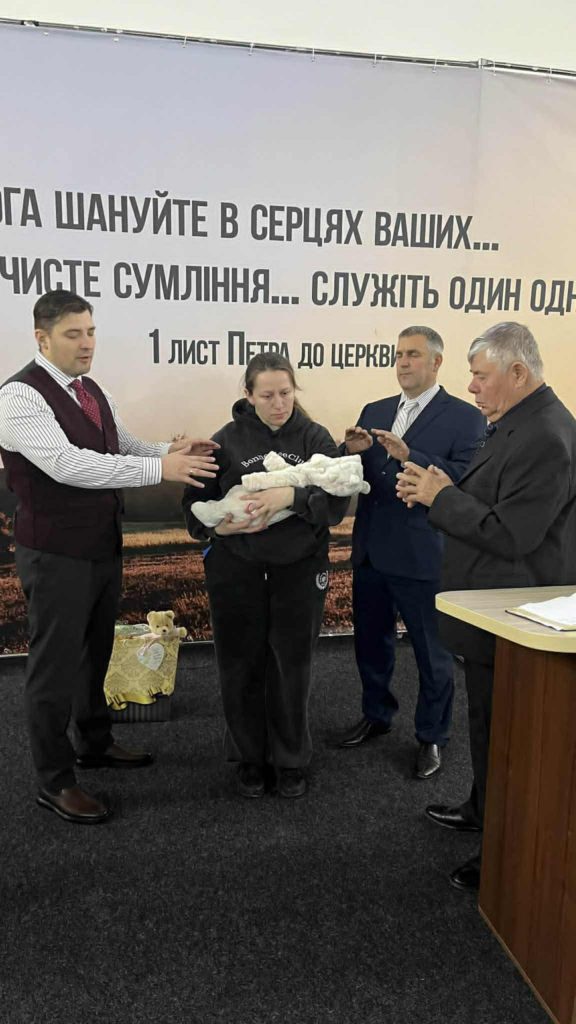 A mother holding her infant while three church leaders pray over them during a baby dedication ceremony.