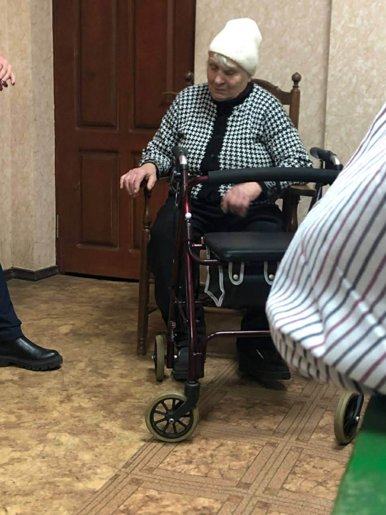 Elderly woman with a mobility walker receiving assistance inside a home.