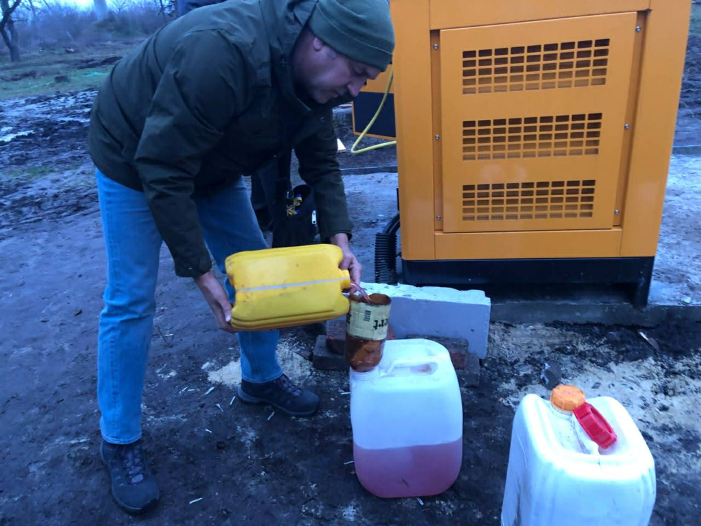 Man pouring fuel from a yellow container into a larger canister beside a yellow generator outdoors.