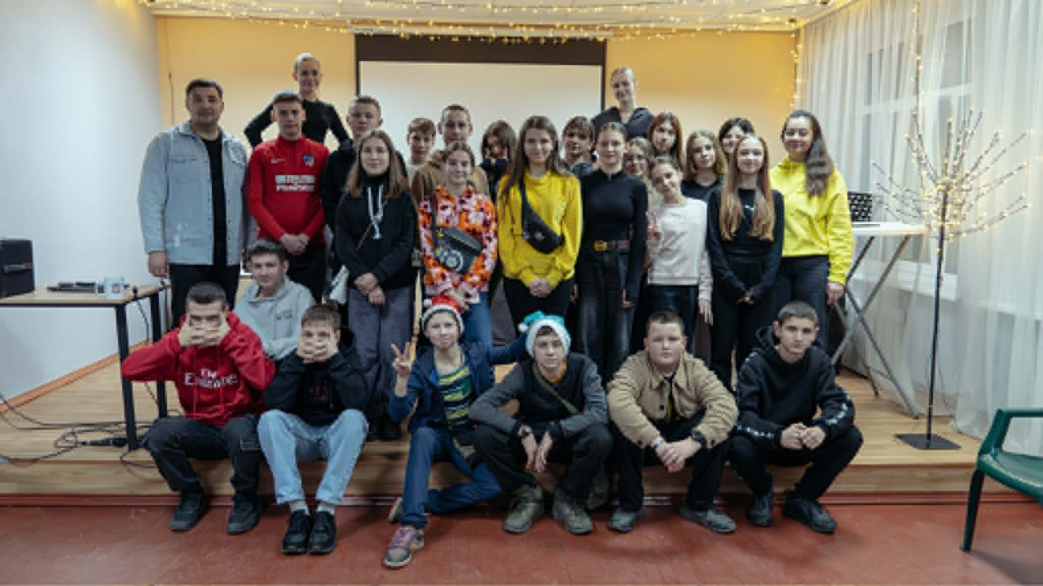 Large group of teenagers and youth workers posing together for a group photo in a decorated room with string lights.