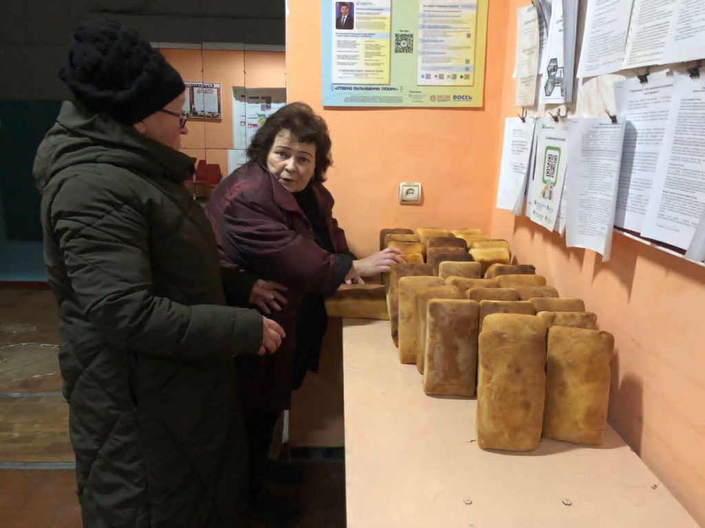 Two women selecting loaves of bread laid out on a counter at a distribution point