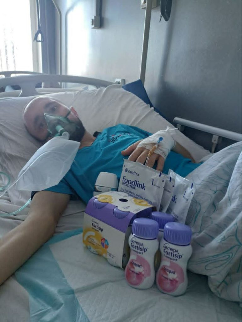 A patient lying in a hospital bed receiving nutritional supplements during a hospital visit.