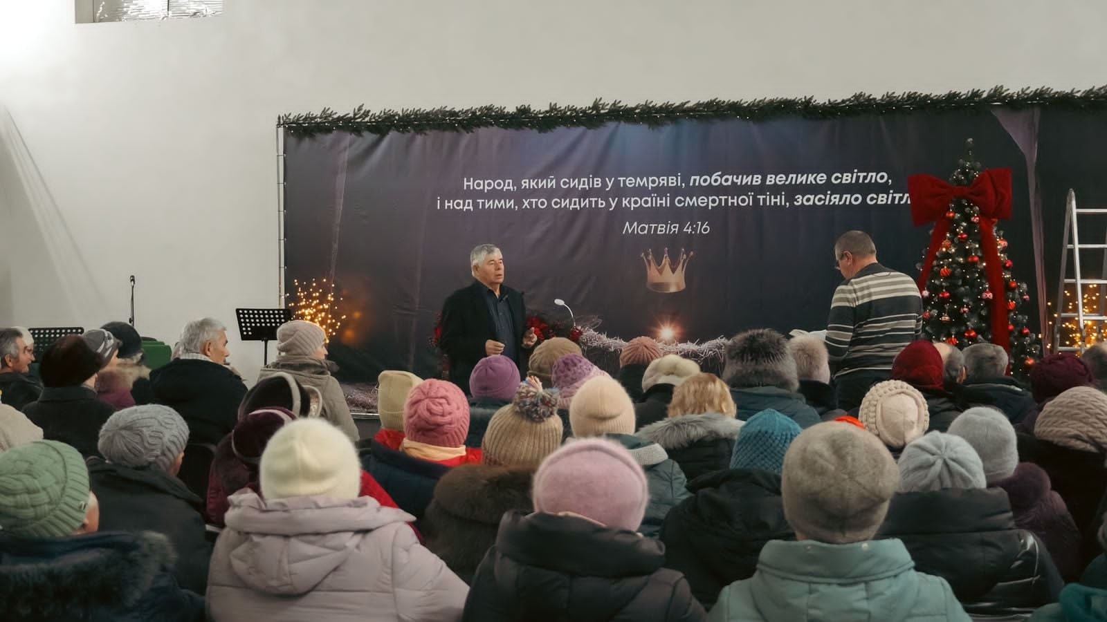 Crowd of internally displaced people attending a service, many wearing winter hats