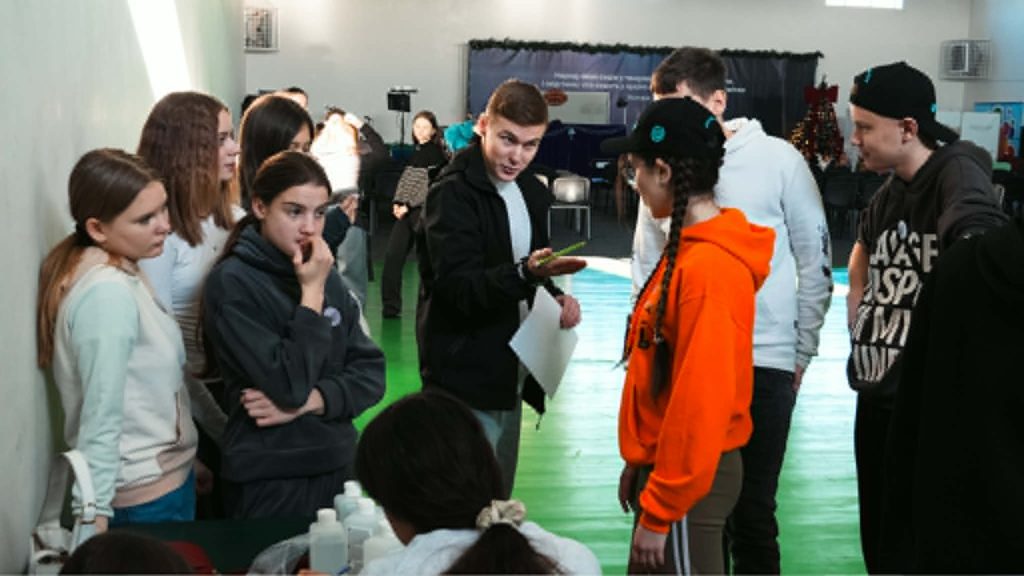Teenagers gathered indoors taking part in a group activity, with one youth explaining something to others.