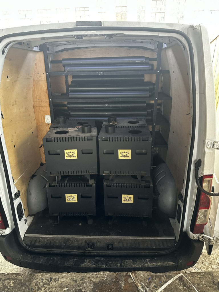 The rear of a delivery van filled with wood-burning stoves and flue pipes, ready to be transported to families in need.