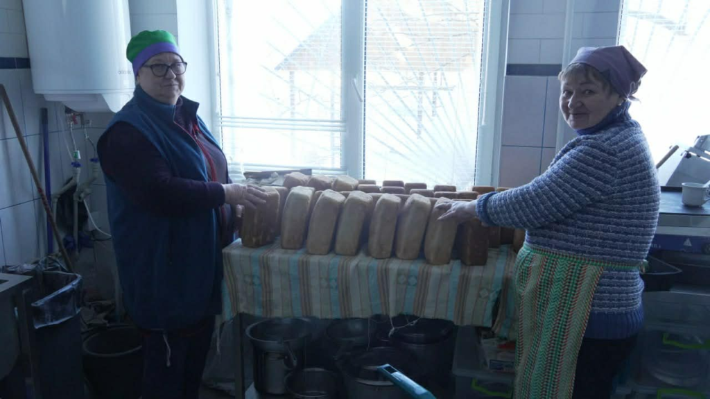 Two women in the bakery kitchen standing behind a table lined with freshly baked loaves of bread.