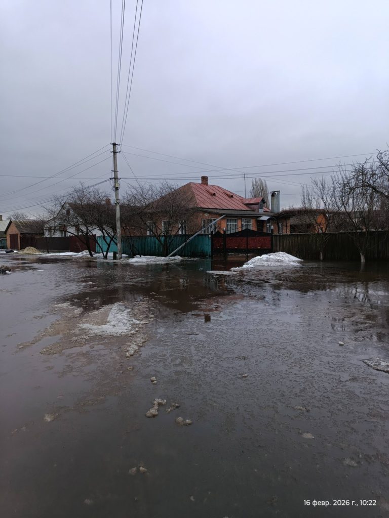 A flooded village street with homes partially surrounded by water, showing the scale of damage faced by families after flooding.