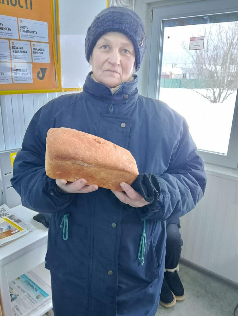 Woman receiving a loaf of fresh bread through a charity food distribution in a rural village near Samotoivka.