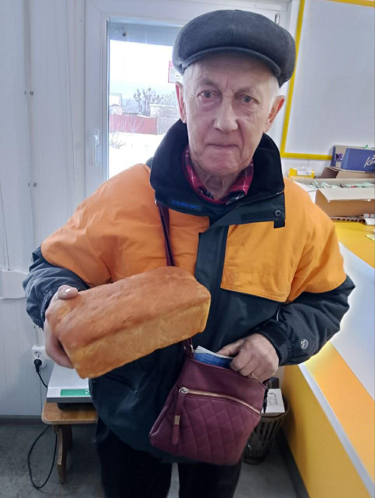 Elderly man holding a loaf of bread provided by the team.