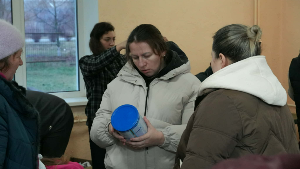 Luda examines a container of supplies while standing with others indoors during an aid distribution