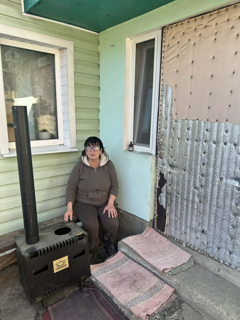 Lyuba sits outside her home beside a newly installed wood-burning stove provided to help her keep warm during winter.