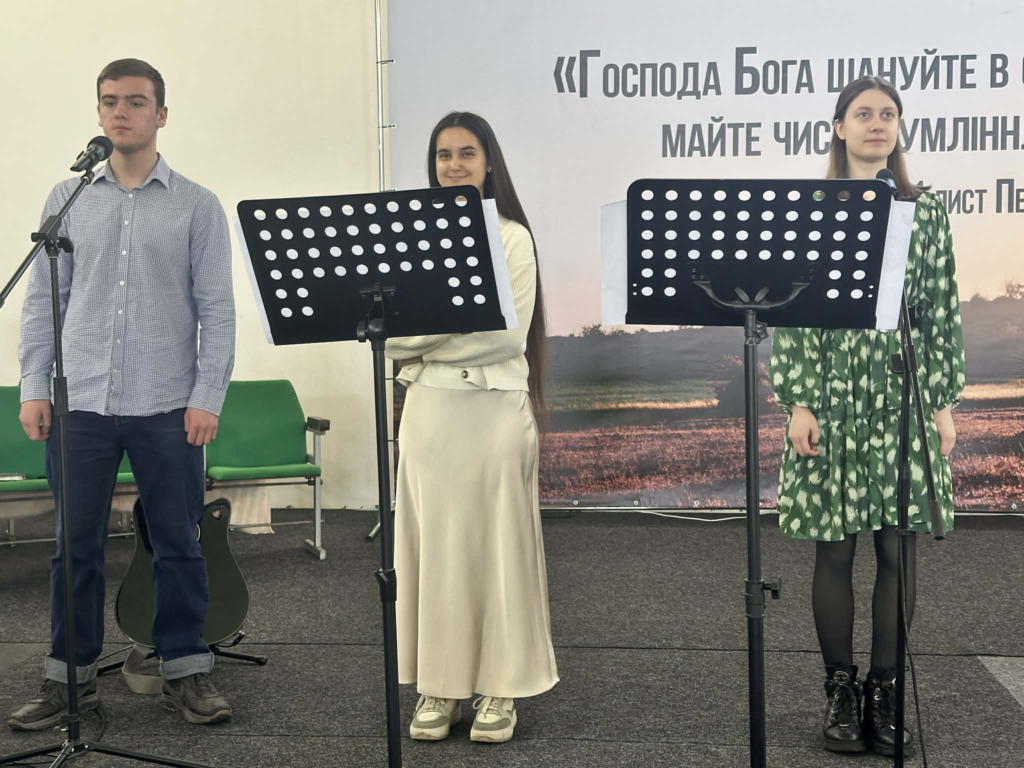 Three young people stand singing at microphones during a church service.