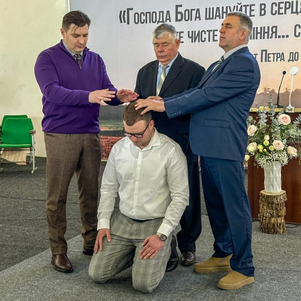 Church leaders pray and lay hands on Valentine during his ordination as a deacon in the church.