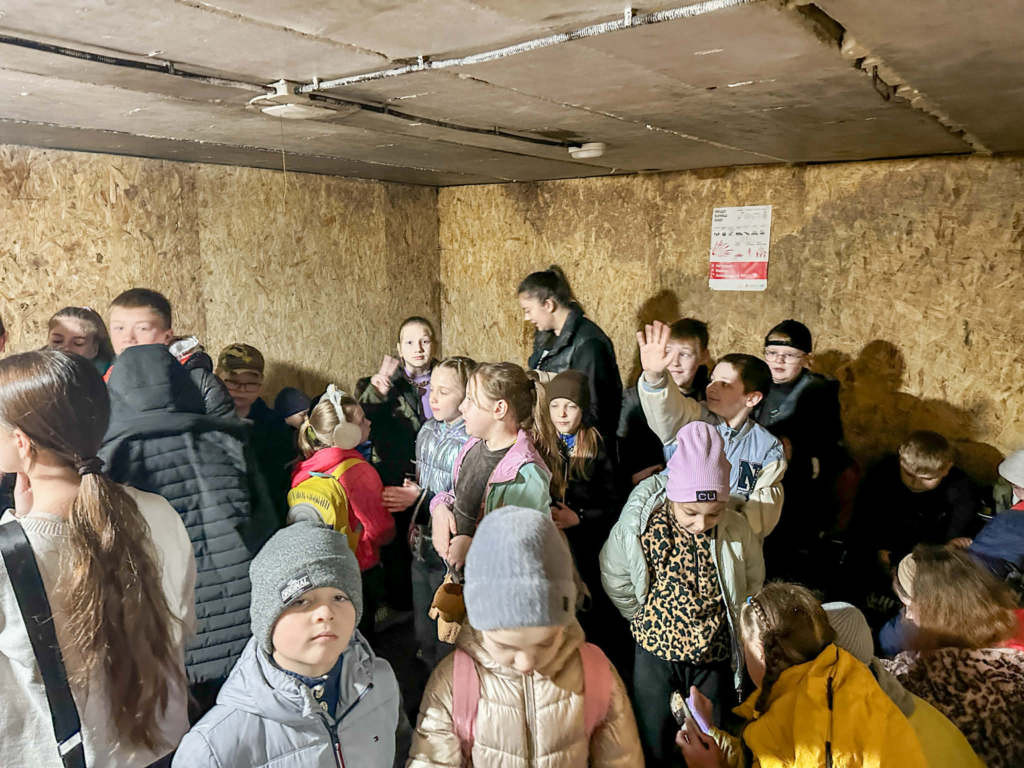 A crowded group of children stand together inside the bomb shelter at the Centre, wearing winter clothing during the Easter camp.