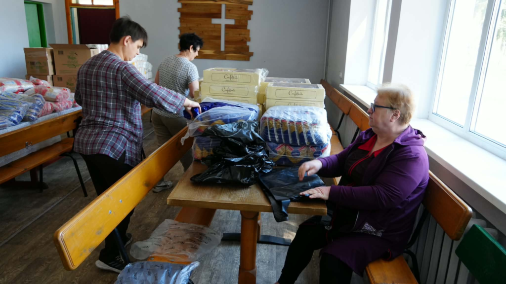 Volunteers sort and package food and household supplies inside the Centre with boxes and donated items on tables.