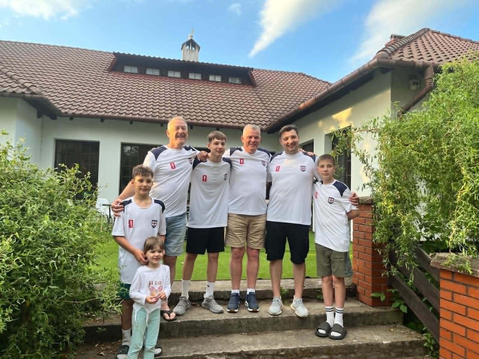 All the boys together in matching football shirts standing on steps with a house behind.