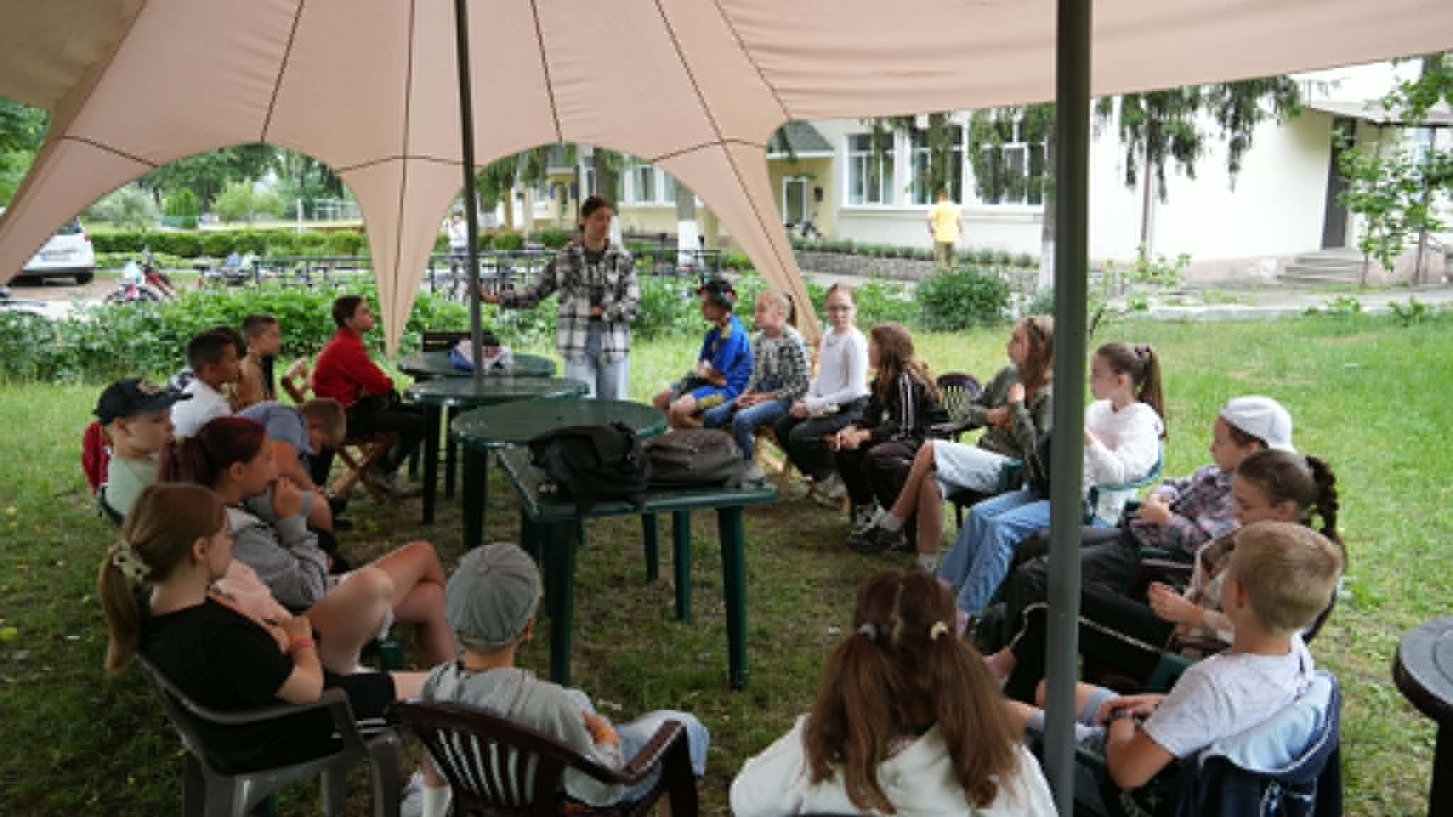Children gather under a canopy for a Bible discussion and group teaching session during a summer camp at the Centre.