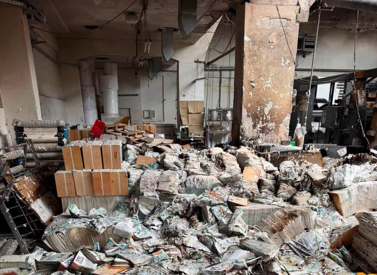 Bomb-damaged interior of an educational book publisher, with piles of burnt and water-damaged books covering the floor.