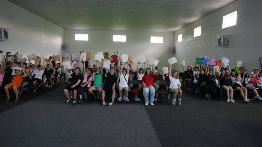 Teenagers celebrate the end of summer camp, proudly holding up backpacks, gifts and prizes they received during the closing session.