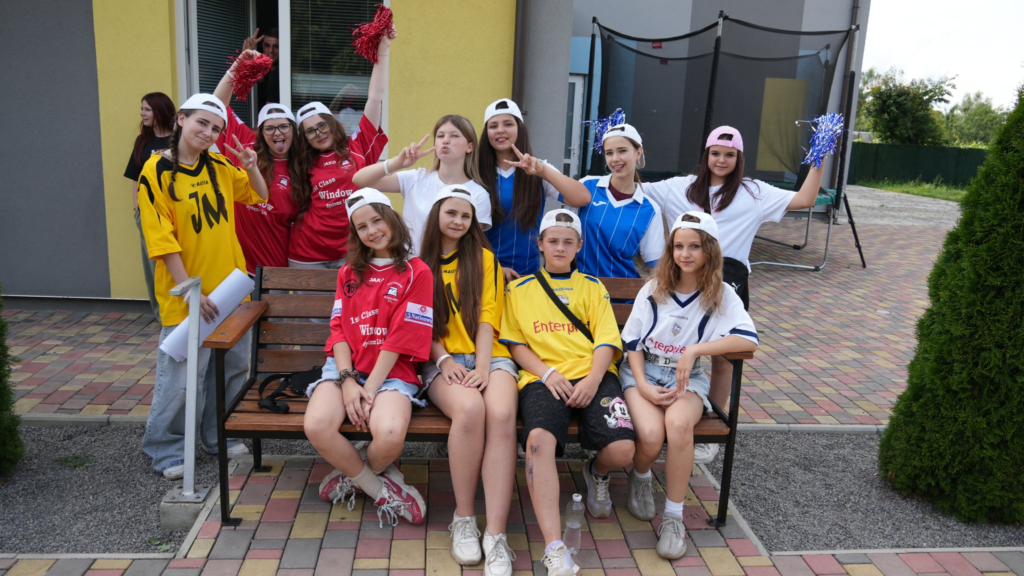 Teenagers dressed in colourful team shirts and caps pose together outside during a fun team competition at summer camp.