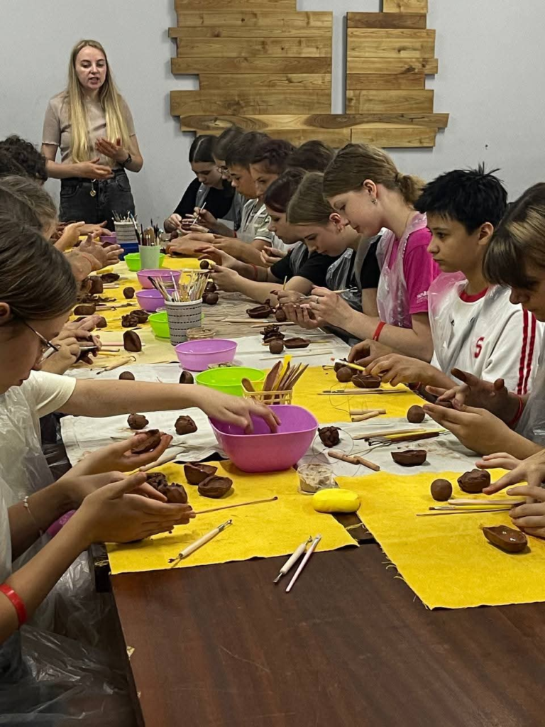 Teenagers taking part in a clay-modelling activity at a long table during the summer camp.