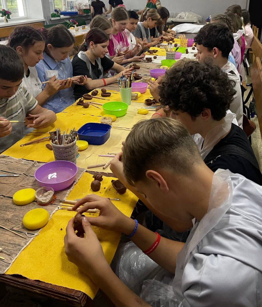Teenagers concentrating on shaping and decorating clay models during a summer camp craft session.
